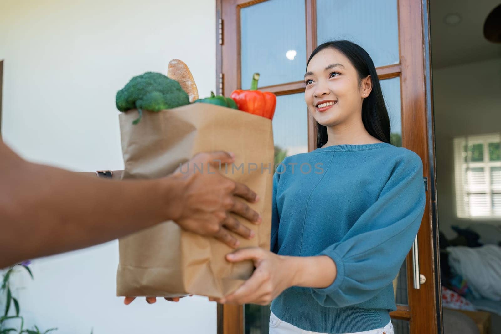 Asian deliver man worker handling bag of food, fruit, vegetable give to young beautiful female in front of the house by itchaznong