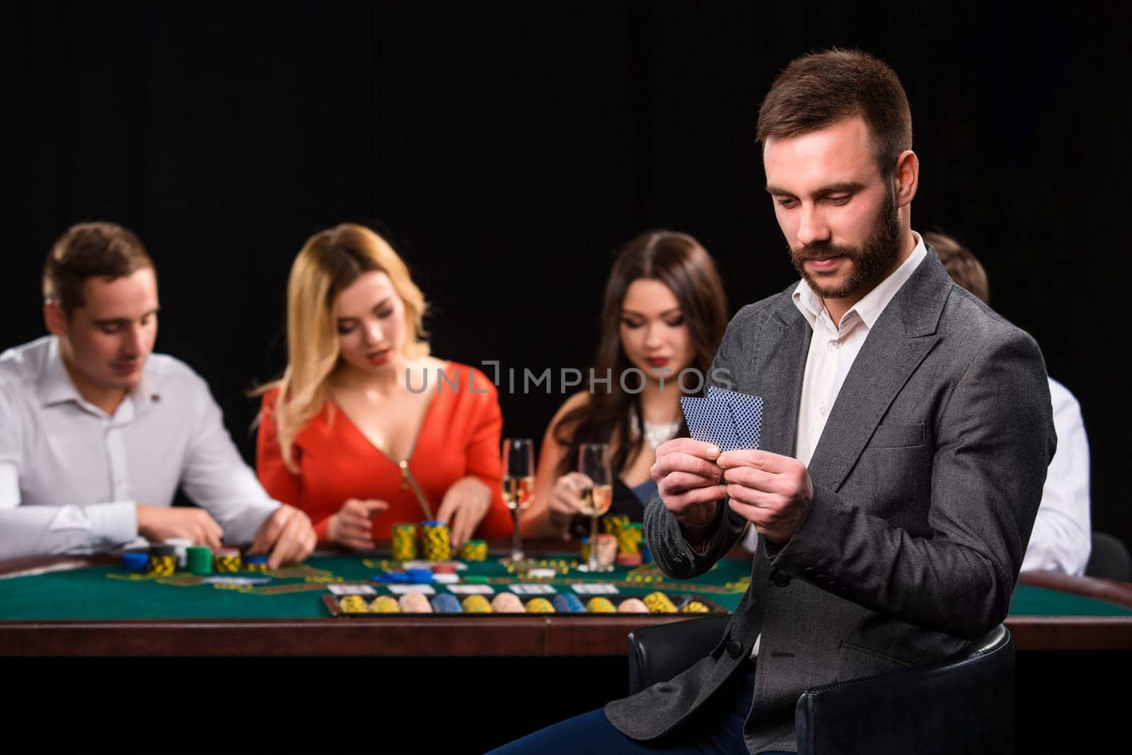 Poker players in casino with cards and chips on black background. A handsome man in the foreground, behind a game table.