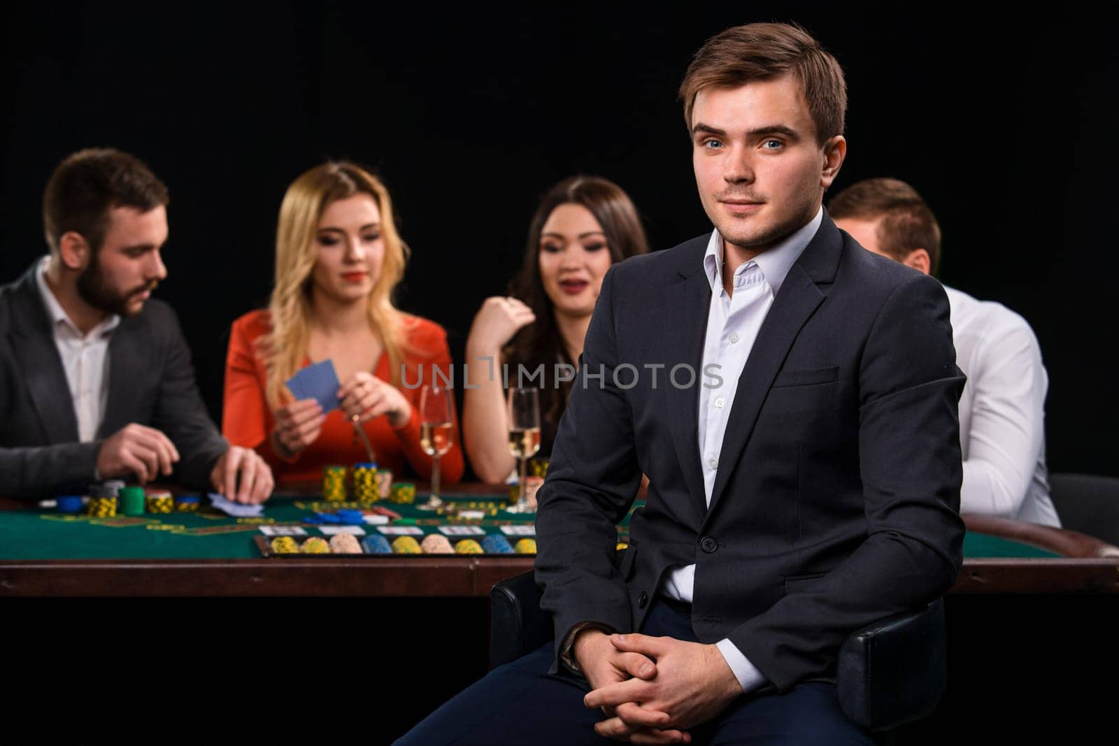 Young people playing poker at the table. Handsome man sitting in the foreground. Casino