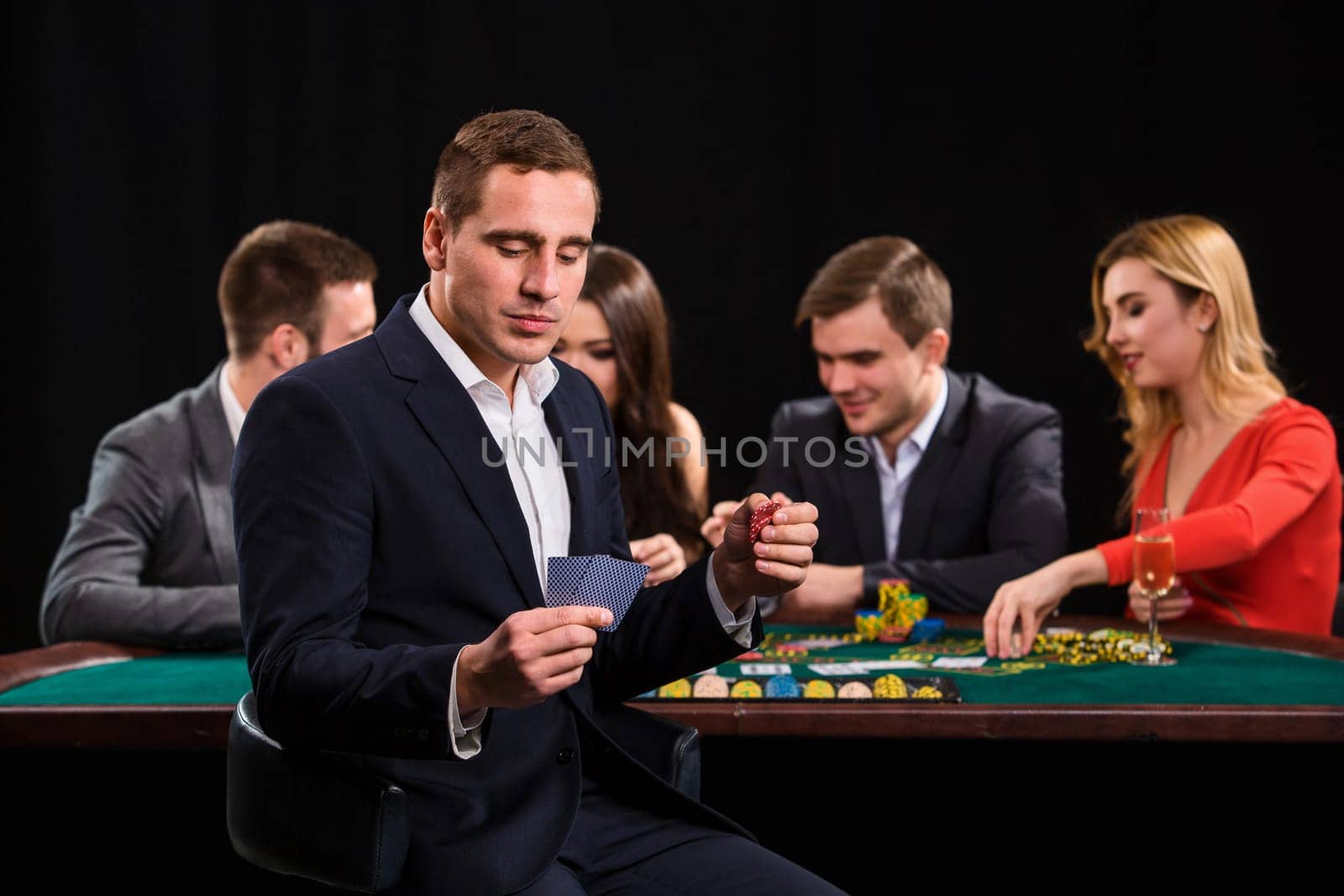 Poker players in casino with cards and chips on black background. A handsome man in the foreground, behind a game table.