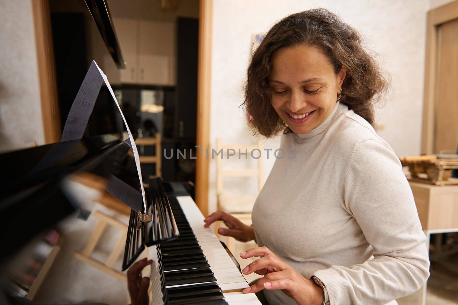 Happy African American woman smiling while playing grand piano, feeling the rhythm of classic music while touching ebony and ivory wooden keys. Female musician practicing the chord musical instrument