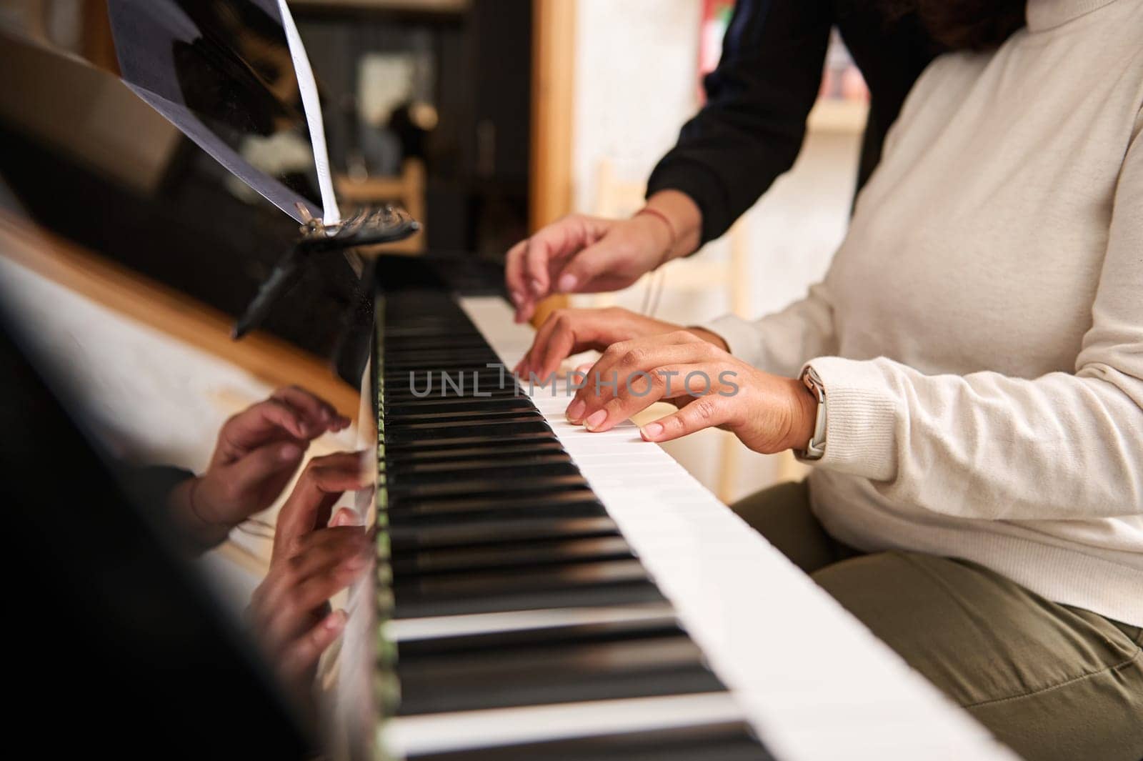Female hands playing grand piano under the guidance of a music teacher. Close-up fingers touch ebony and ivory piano keys. Photo shot with perspective. People. Music. Arts, culture and entertainment