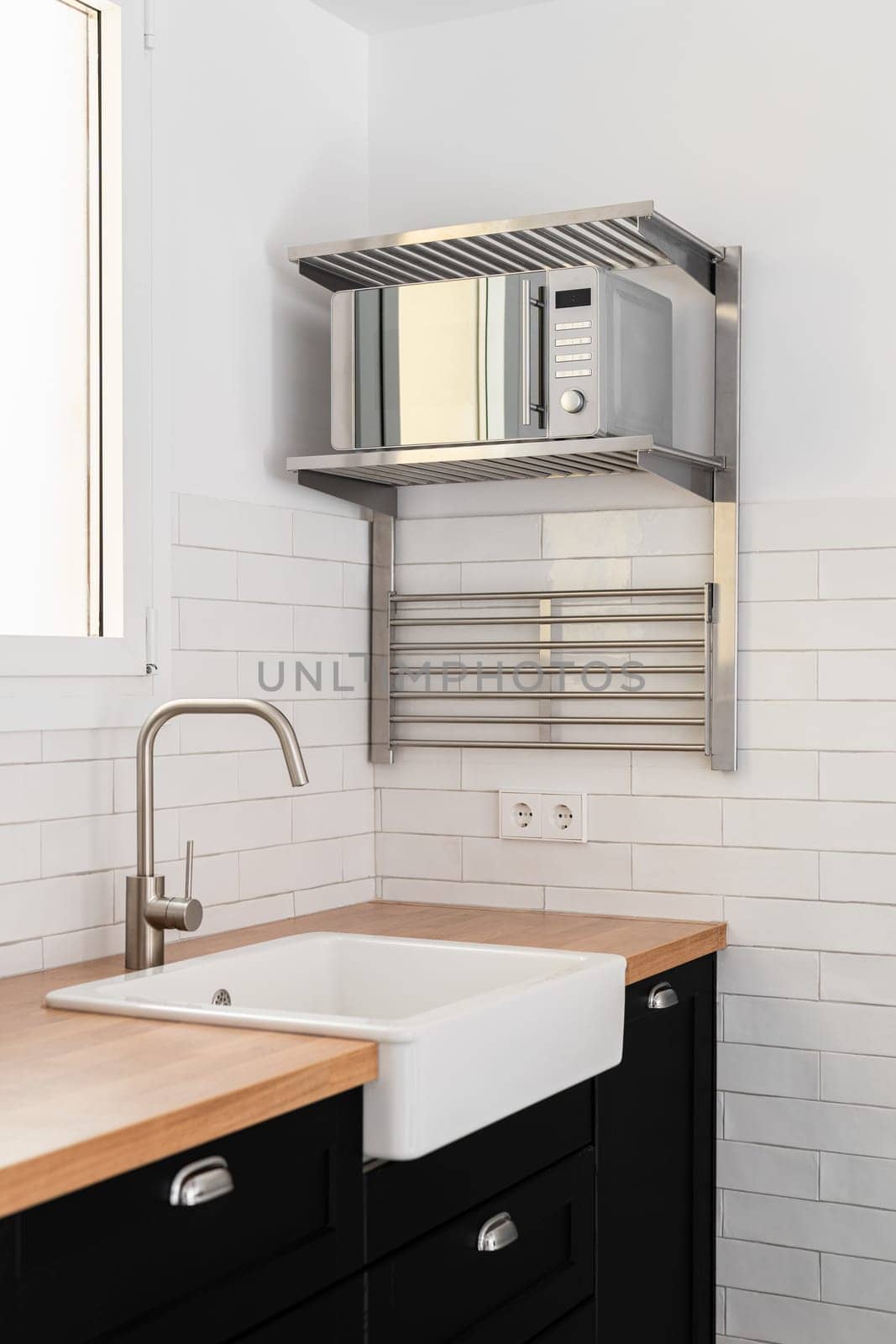 View of a white modern kitchen sink with dark countertops and cabinets and rails and white tiles on window background. The concept of a modern kitchen in a new building by apavlin