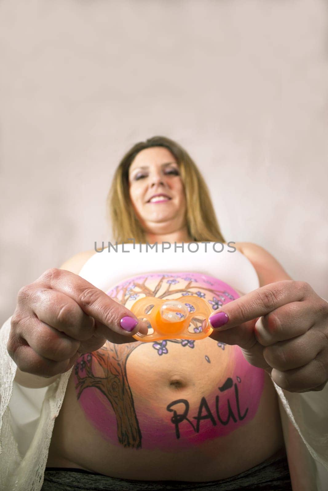 Eight month pregnant woman holding a pacifier in orange color