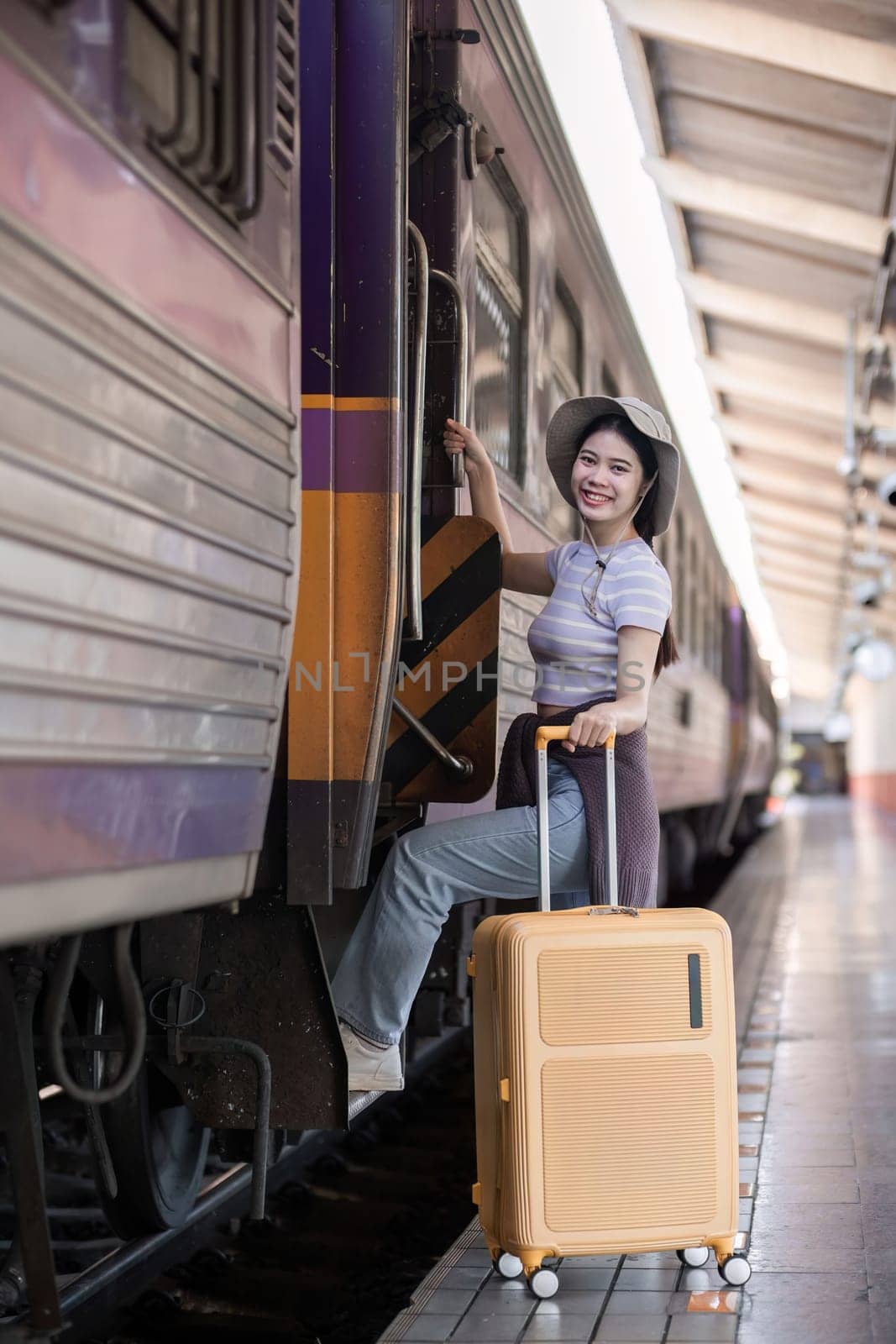 Cute Asian traveler woman carrying a suitcase waiting for the train at the train station by wichayada