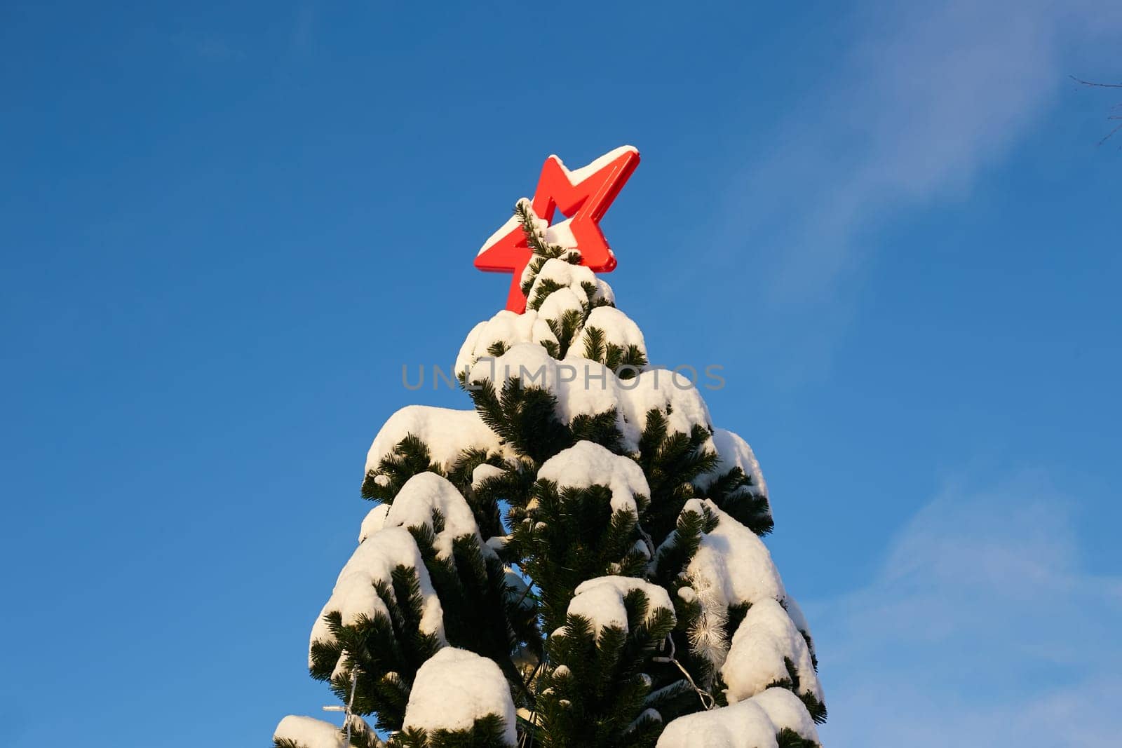Photo a snow-covered fir tree with a red star on a blue sky background. Winter. The party.