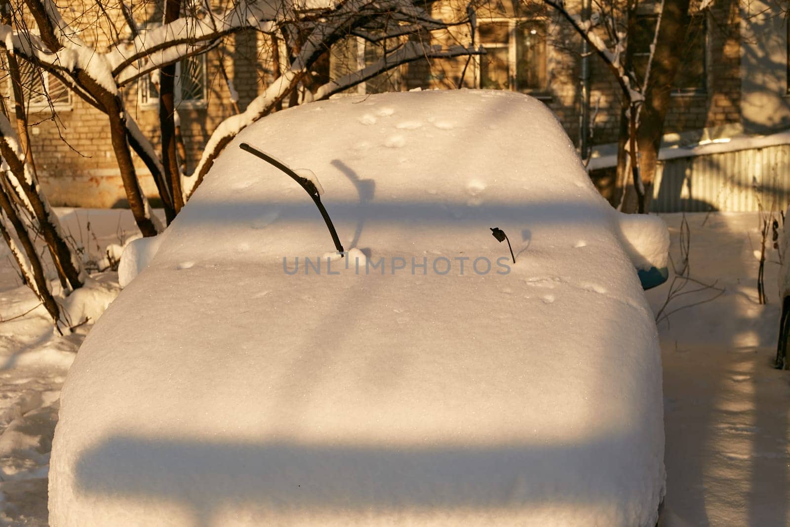 Photo of a car in the snow with the wipers raised. Against the background of a brick house. Winter. Snowdrifts. Cold.