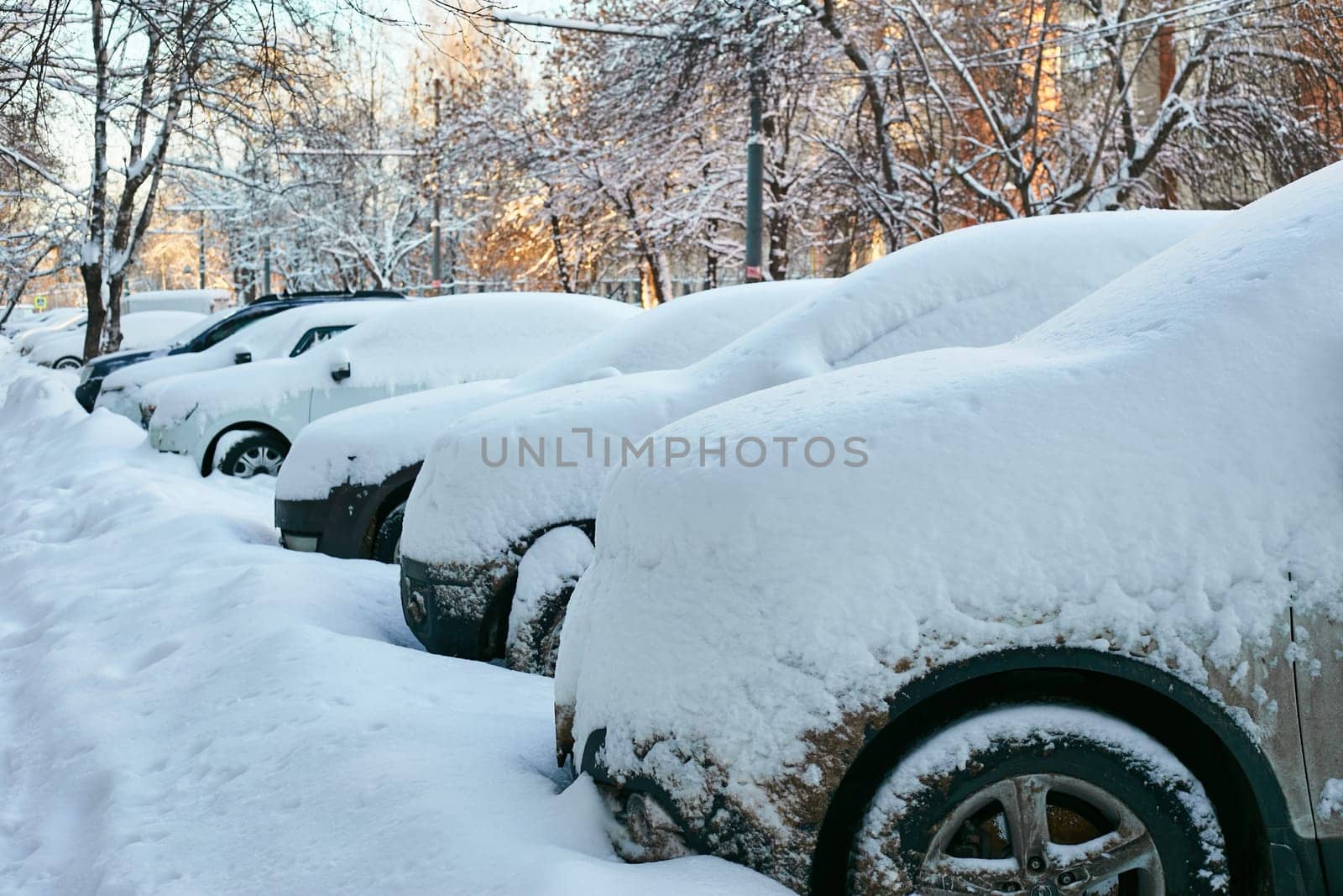 Photo parked cars along the road, snow-covered and uncleaned. Snowdrifts and icing in winter.
