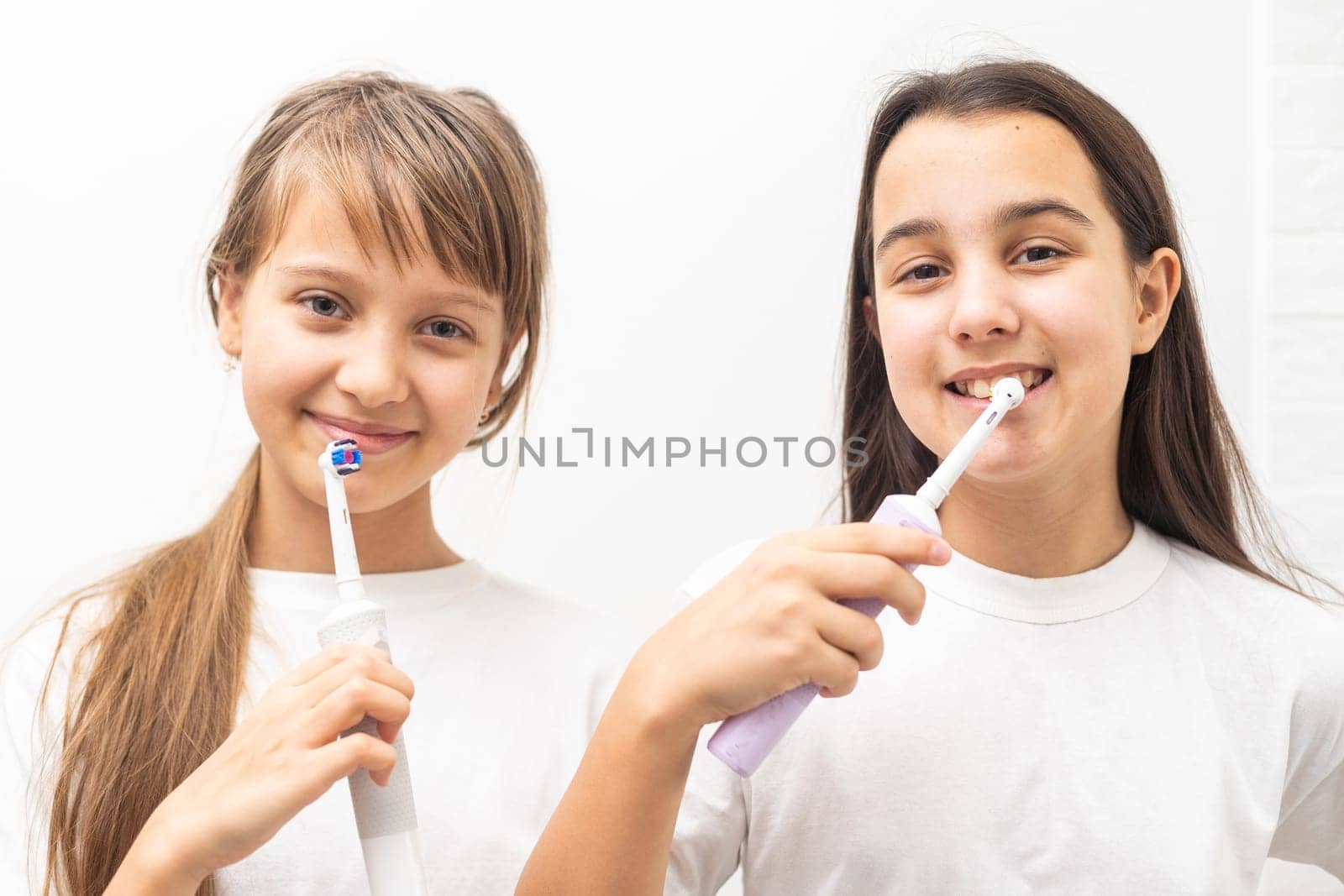 Portrait of two beautiful girls kids with perfect smile holding toothbrushes. Child dental care, oral hygiene concept by Andelov13