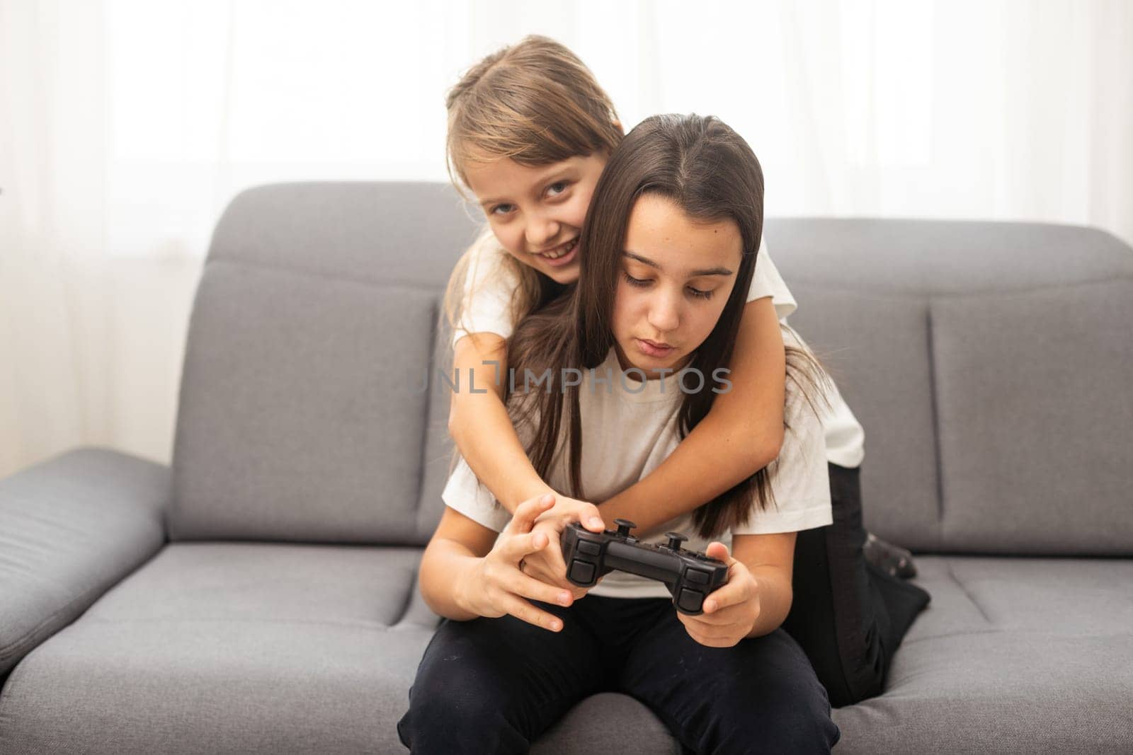 Two little girlfriends playing video game with joysticks. Excited and focused european children. Childhood concept. Entertainment and leisure. Idea of friendship. Grey background in studio. Copy space. High quality photo