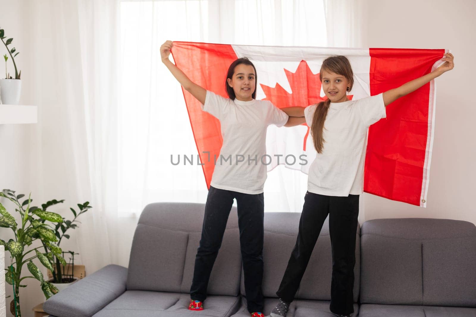 Happy Canada Day Celebration. Two girls with braided hair are at nature background with big Canada flag in their hands. Young Canadian caucasian kids 1st of July. High quality photo