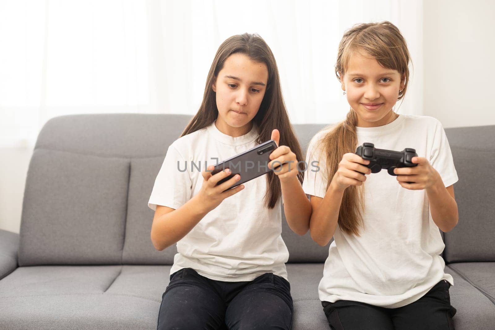 Two sisters kids playing video games at home together. Happy childeren, carefree childhood concept by Andelov13
