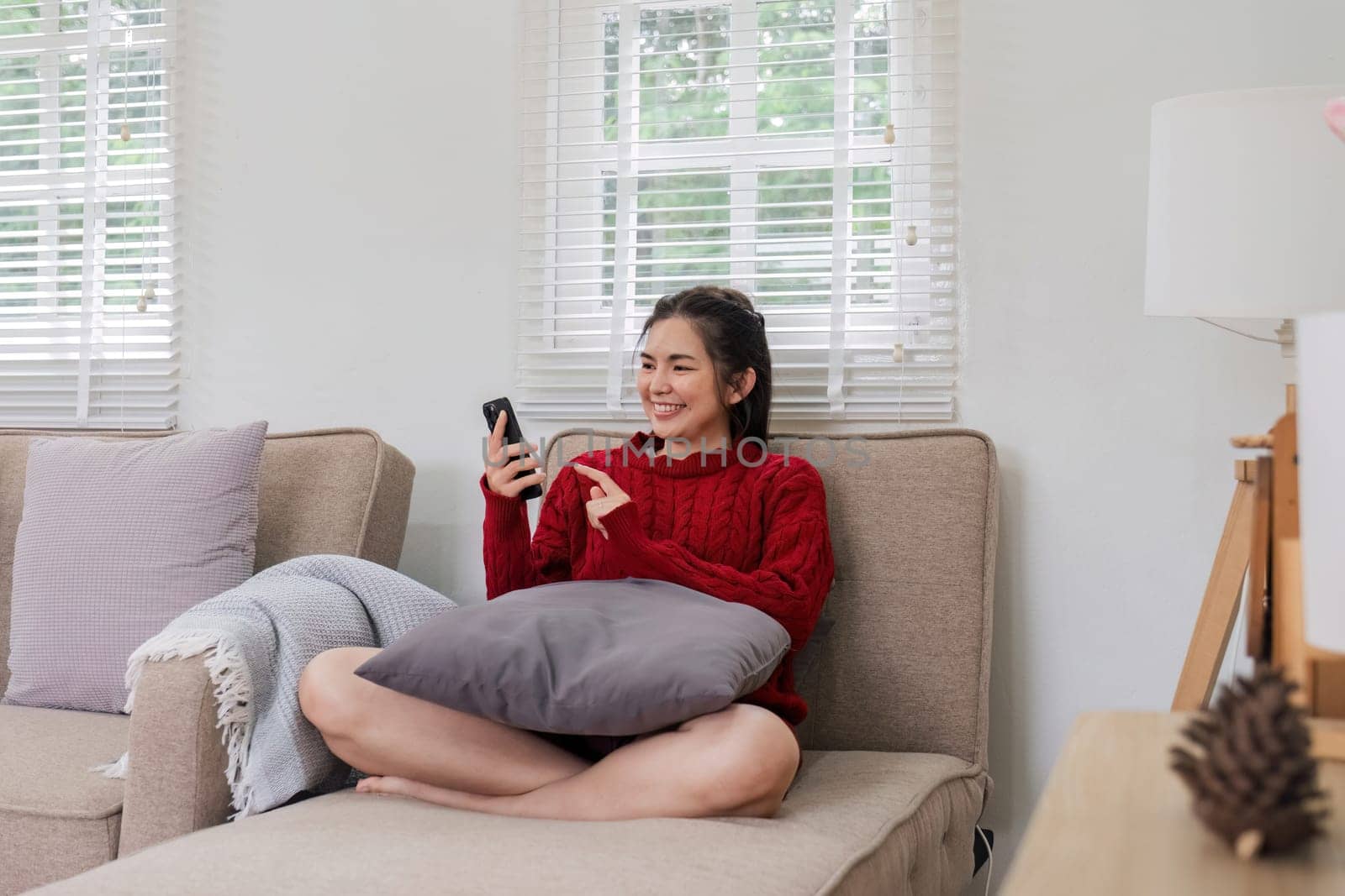 Happy young Asian woman relaxing on a soft sofa. At home, send messages via smartphone. Smiling young woman using a mobile phone online message chat Buy things online from home.