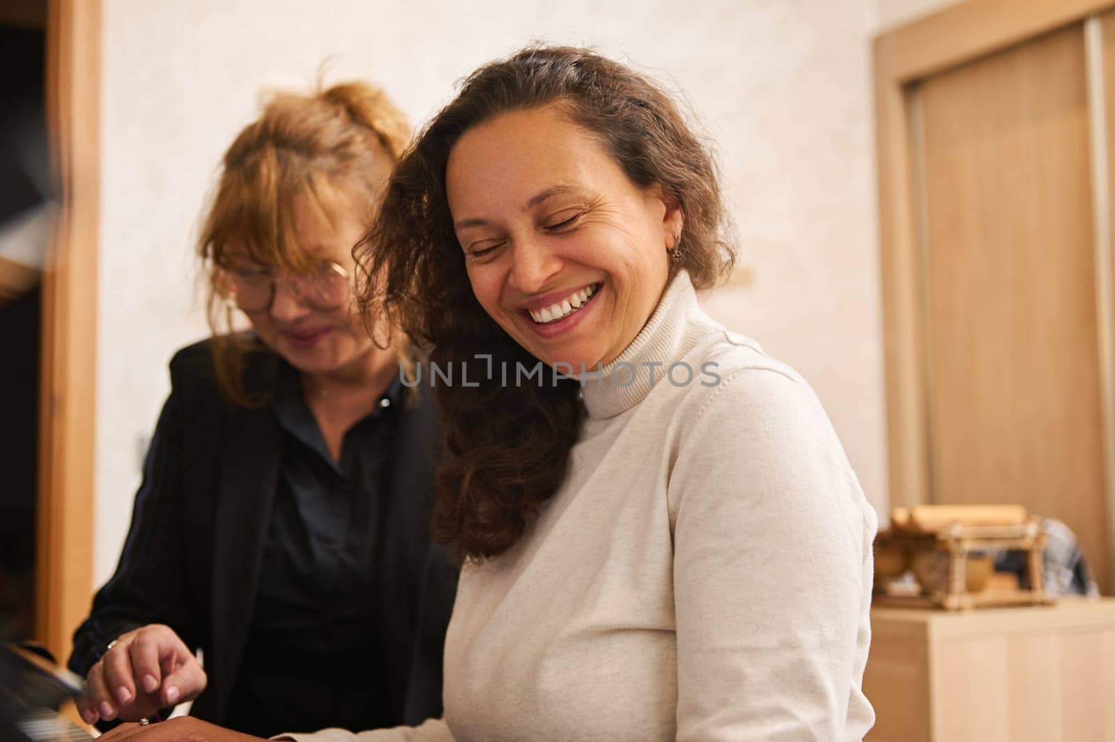Happy women enjoy playing music on grand piano during individual music lesson indoor. African American young adult woman smiling broadly while learning playing on chord musical instrument