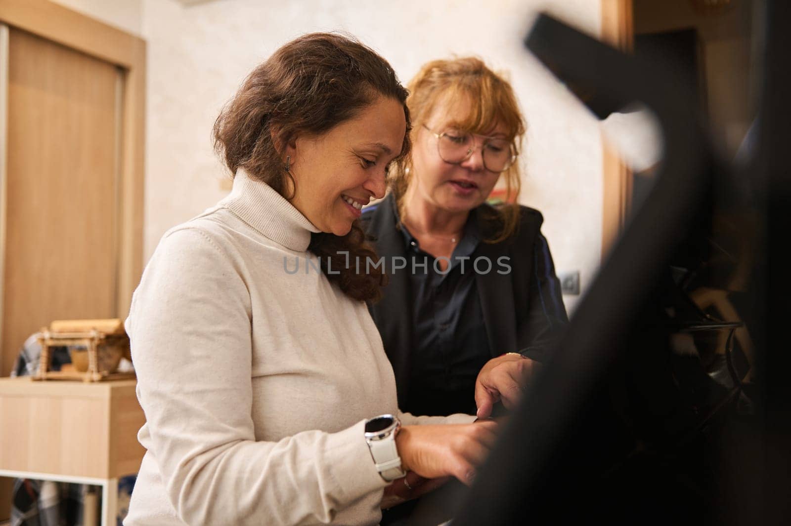 Diverse women feeling the rhythm of music while performing classic melody on grand piano, during individual music lesson. People, hobbies and lifestyle