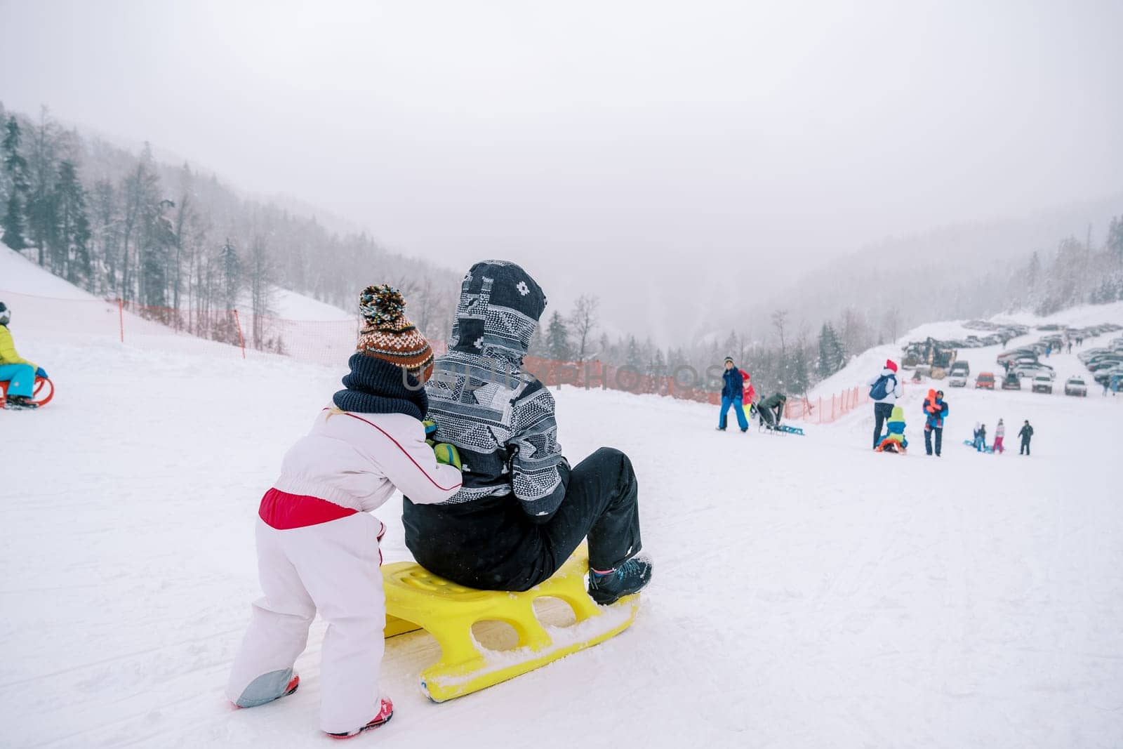 Small child pushes his mother down the mountain on a sled. Back view. High quality photo