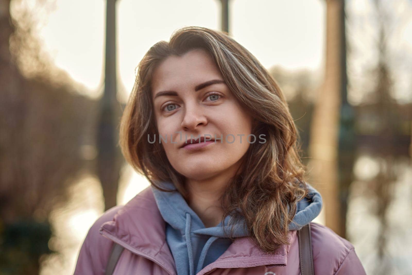 A young woman standing at the shore looking at the river in autumn sunny day. Street view, copy space for text, travel photo. Happy tourist woman on the bank of the river in autumn in warm clothes. Tourists enjoy their vacation, winter season. Romantic look and travel concept. A joyful mood in a caucasian girl. Winter Wonderland: Enchanting Girl by the Riverside in Autumn by Andrii_Ko