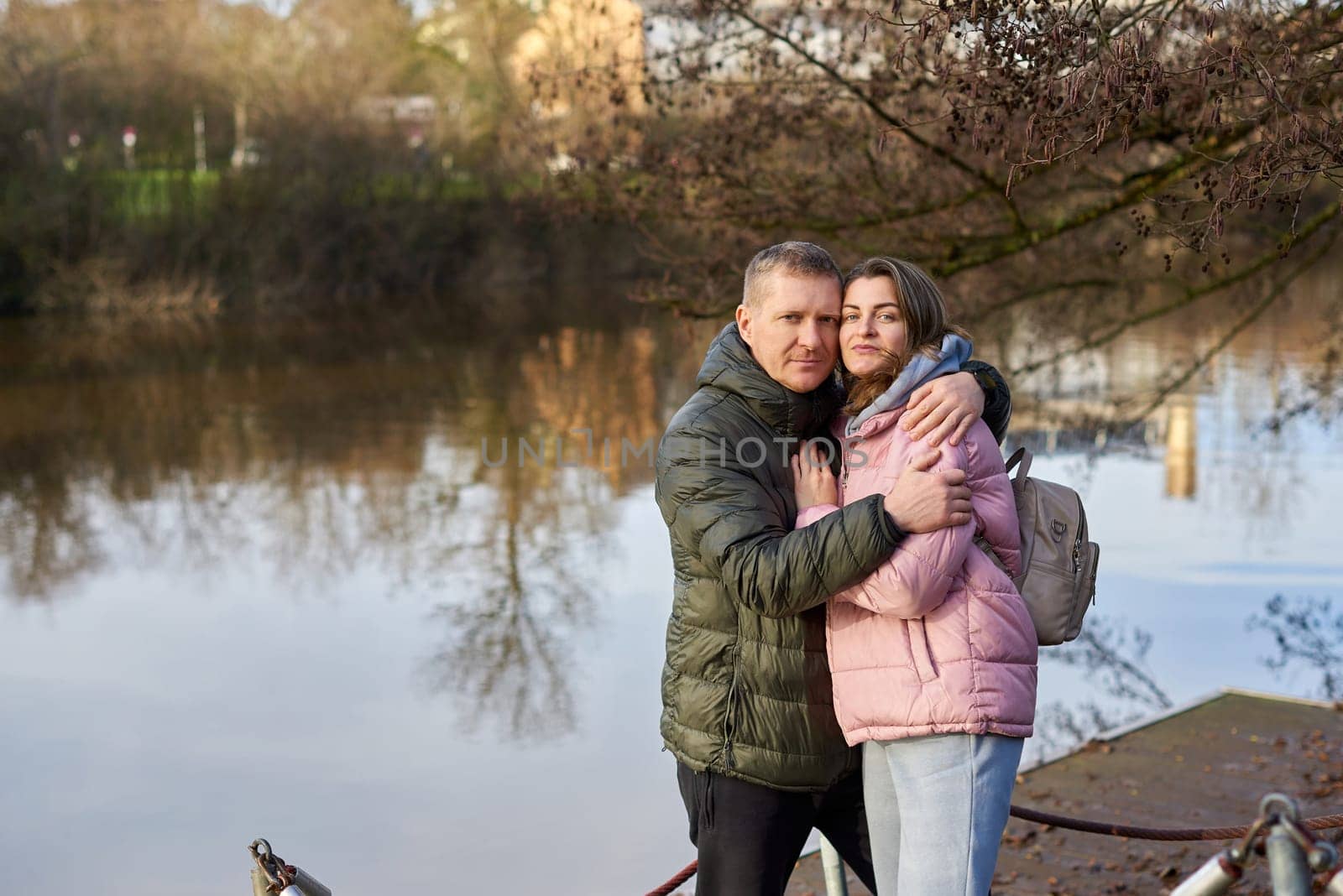 Loving couple sit on the shore of the pond in the park in autumn. A man and a woman. A couple, lovers on the shore of the lake on a walk