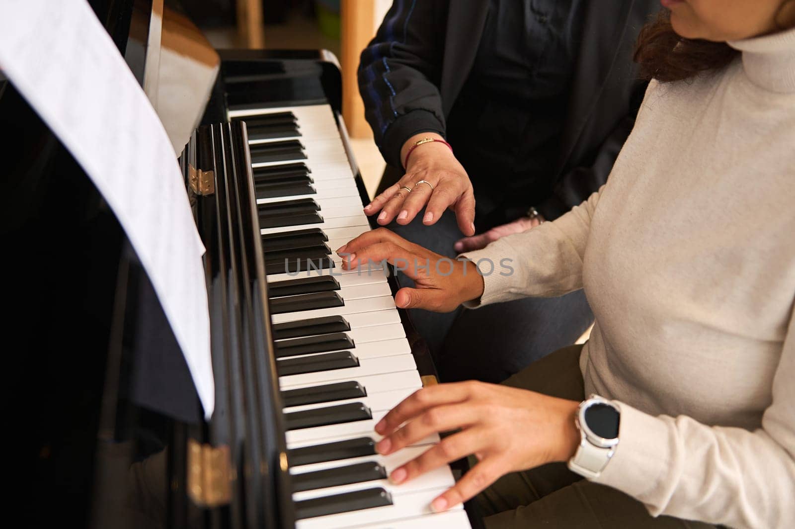 Close-up view of women hands playing piano indoor during music lesson. Female pianist teacher explaining piano lesson, touching white and black piano keys, performing classical music composition