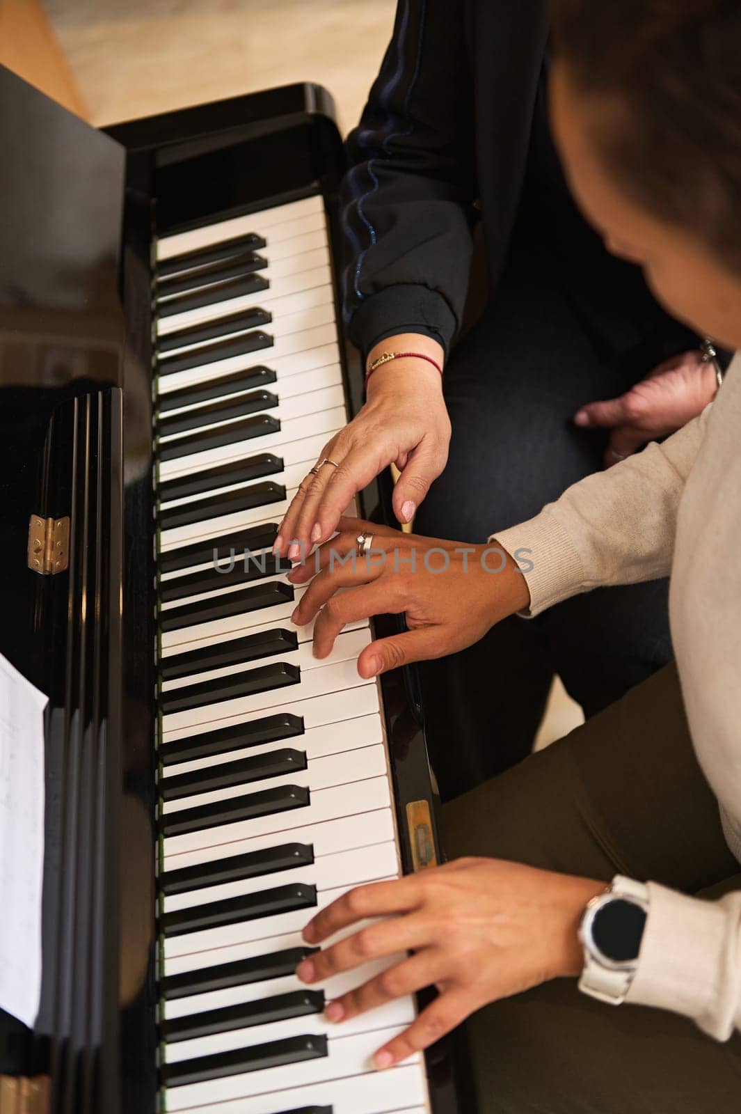 Overhead view of a young woman learning playing piano, touching piano keys under the guidance of her teacher by artgf