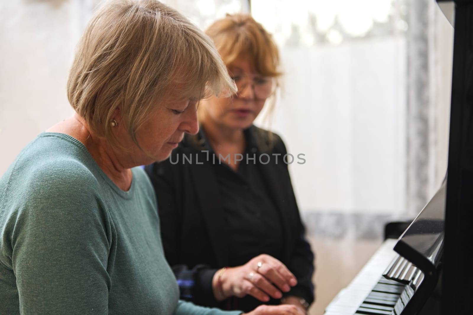 Portrait of two diverse mature women playing piano together at home. Music as therapy.