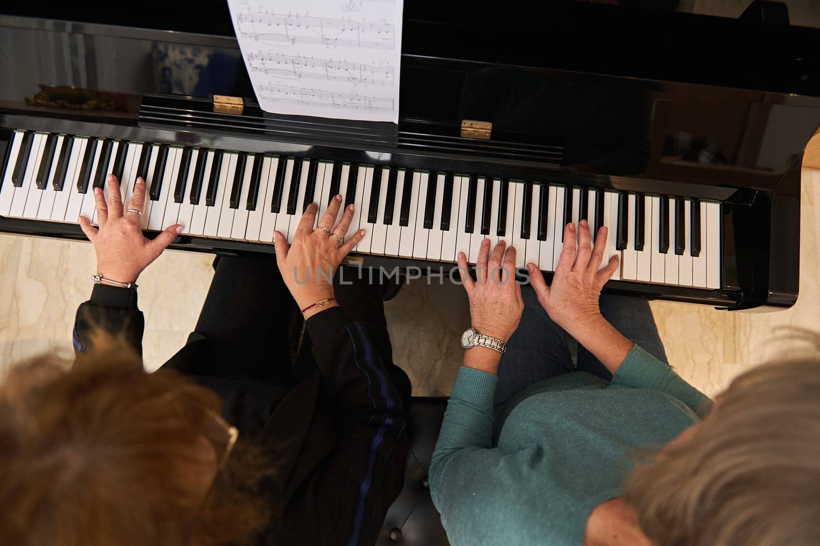 View from above of two pretty women playing the piano in four hands. Confident female pianists musicians are studying a new musical composition and playing the piano at home. Music lesson.