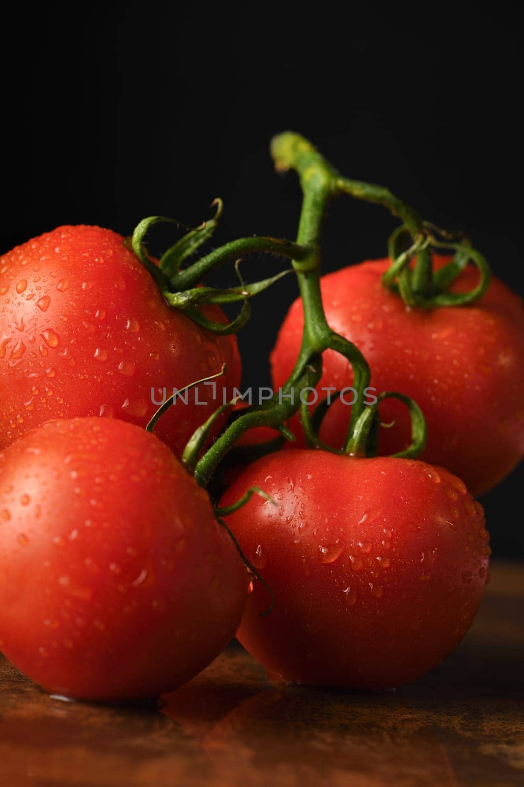 Fresh ripe red tomato branch on a rusty, redhead table with water drops. Dark background. Close-up. Vertical photo. Poster for vegetable market or shop.