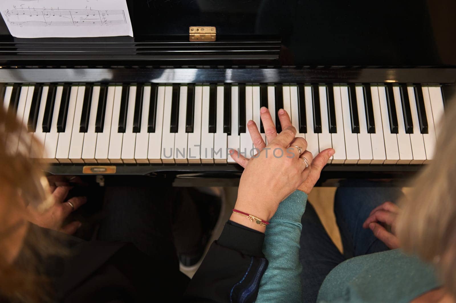 View from above women holding hands on piano ebony and white keys, performing classical musical composition, feeling rhythm while play grand piano at home. Music lessons for adults. People. Education