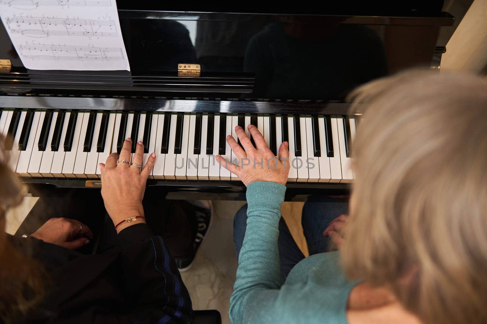 View from above of two multi ethnic mature women playing piano in four hands and organ in home studio by artgf