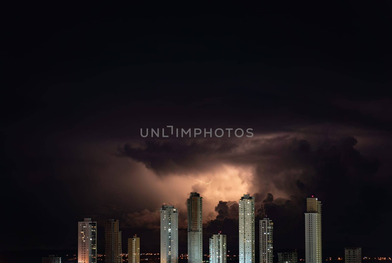 Impressive row of towering skyscrapers with a thunderstorm and lightning bolts above them, perfect for adding text. The buildings dominate the city skyline with their height.