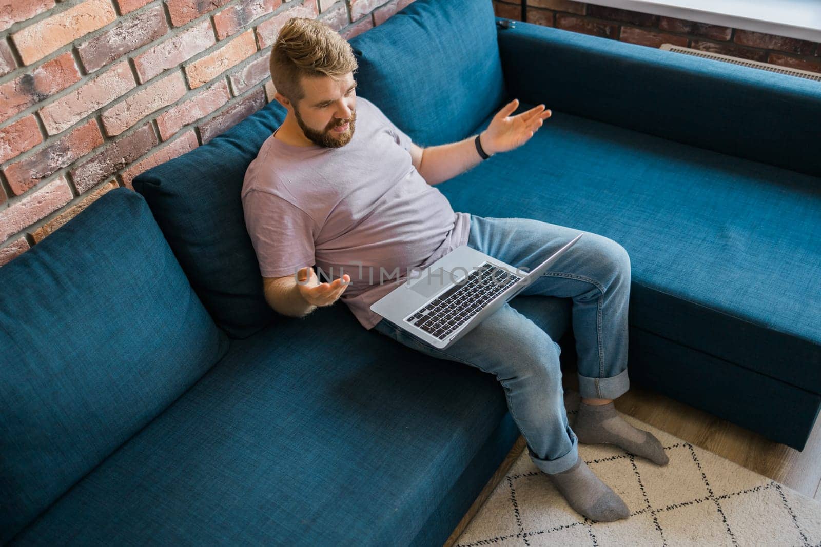 Millennial man at home on couch talking by video call with a laptop. Technologies for freelancer and communication online concept by Satura86