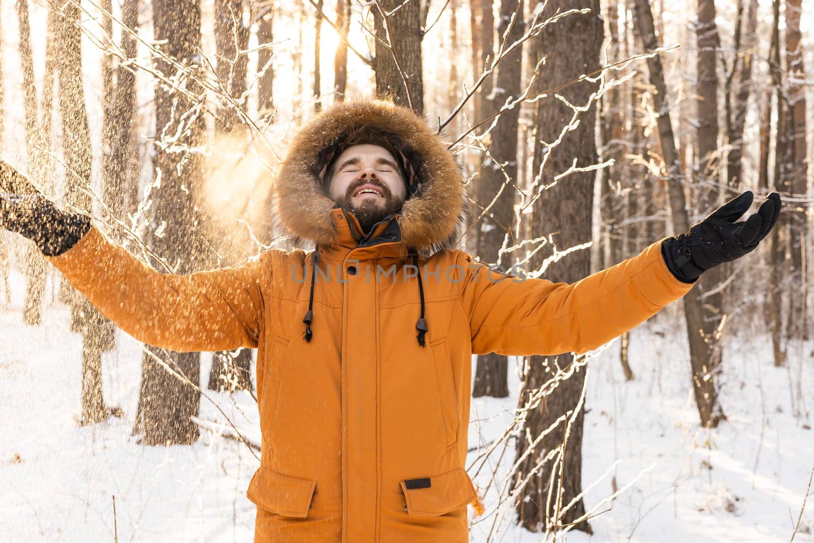 Happy bearded man in hat throws up snow in winter nature. Snowy cold season and holidays lifestyle