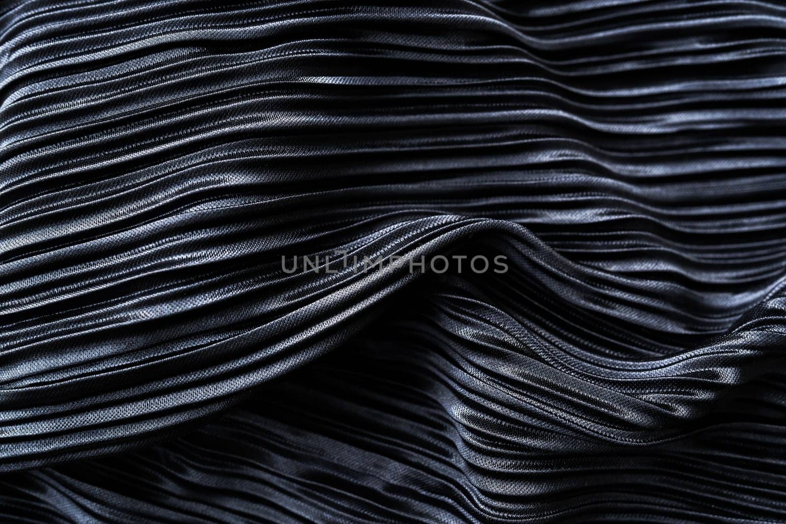 A close-up view of a dark-colored fabric with intricate wavy patterns. The fabric has a glossy finish that reflects light and emphasizes the richness of its color and texture