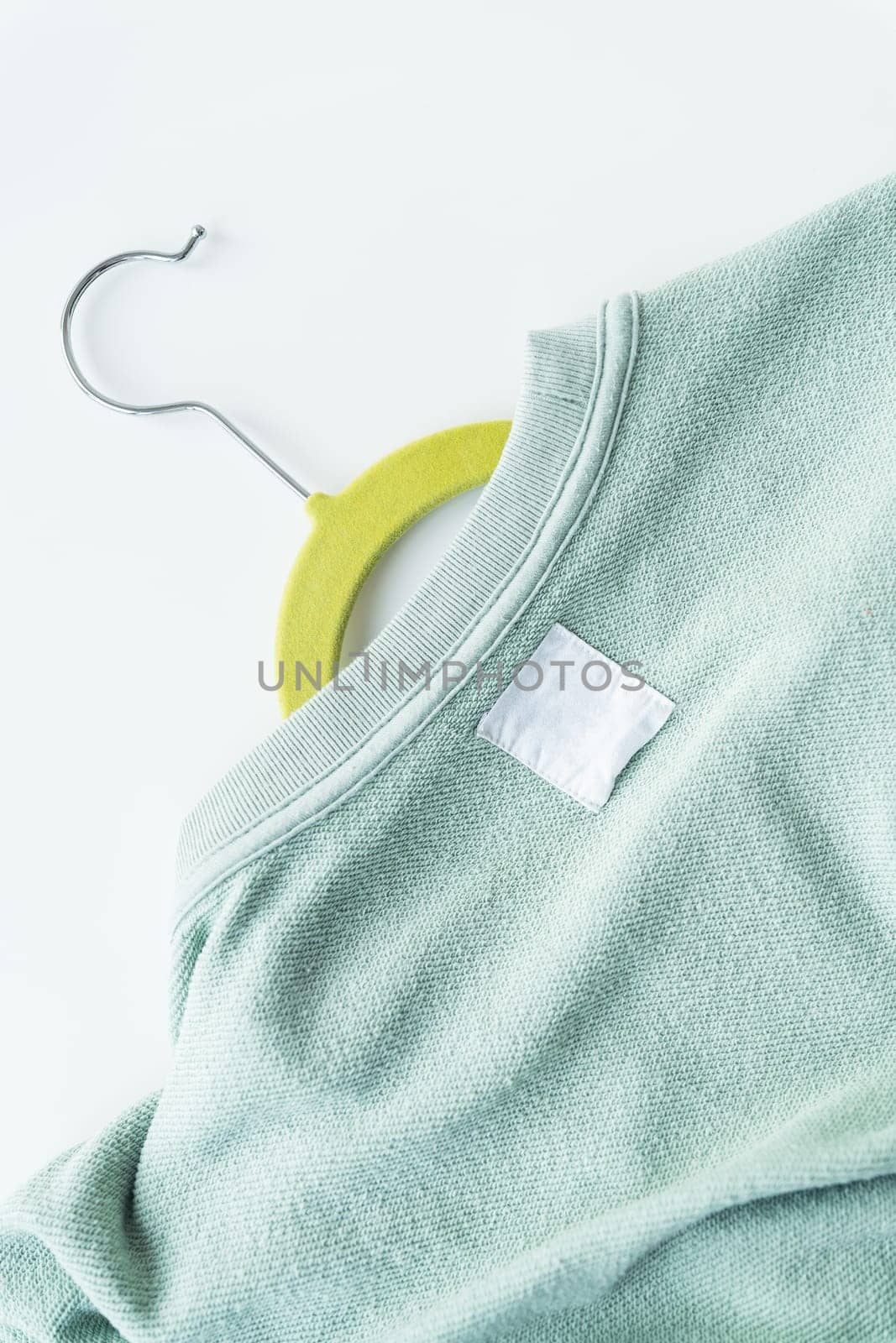 A close-up of a mint green sweater on a yellow hanger. The sweater has a visible texture and a white blank label. The background is plain and white