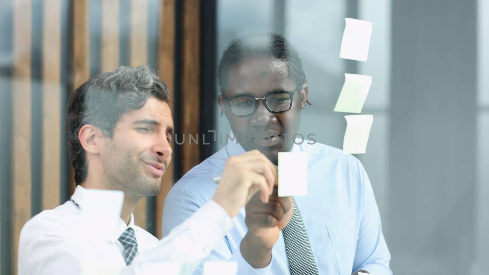 two businessmen discussing business strategy. standing behind the glass looking at stickers by Prosto