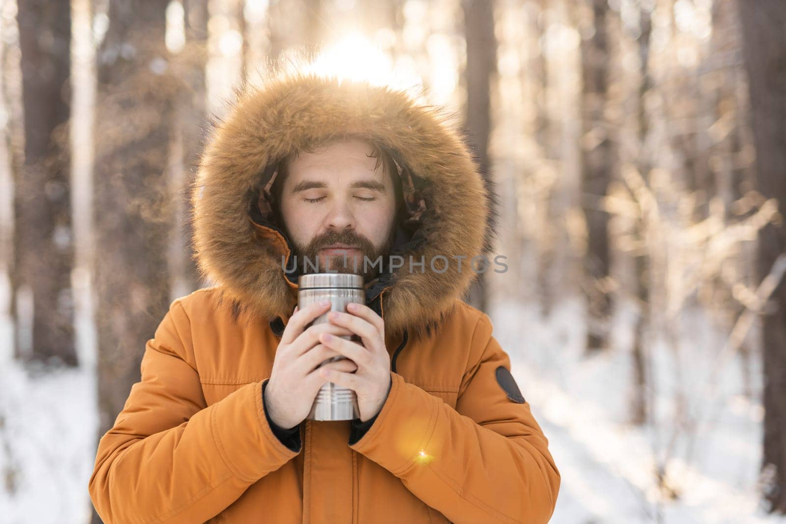 Close-up portrait handsome bearded millennial man in winter clothes and with thermos snow outdoor. Cold season and hot beverage in winter time.