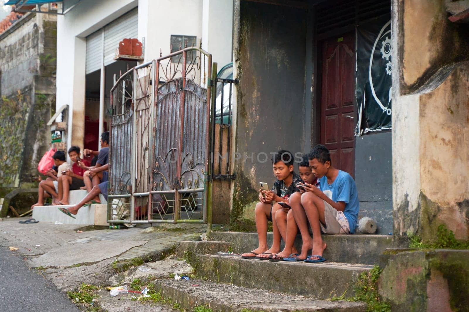 People resting near the road in an unusual Asian village. Children are playing and adults are talking sitting on the roadside. by Try_my_best