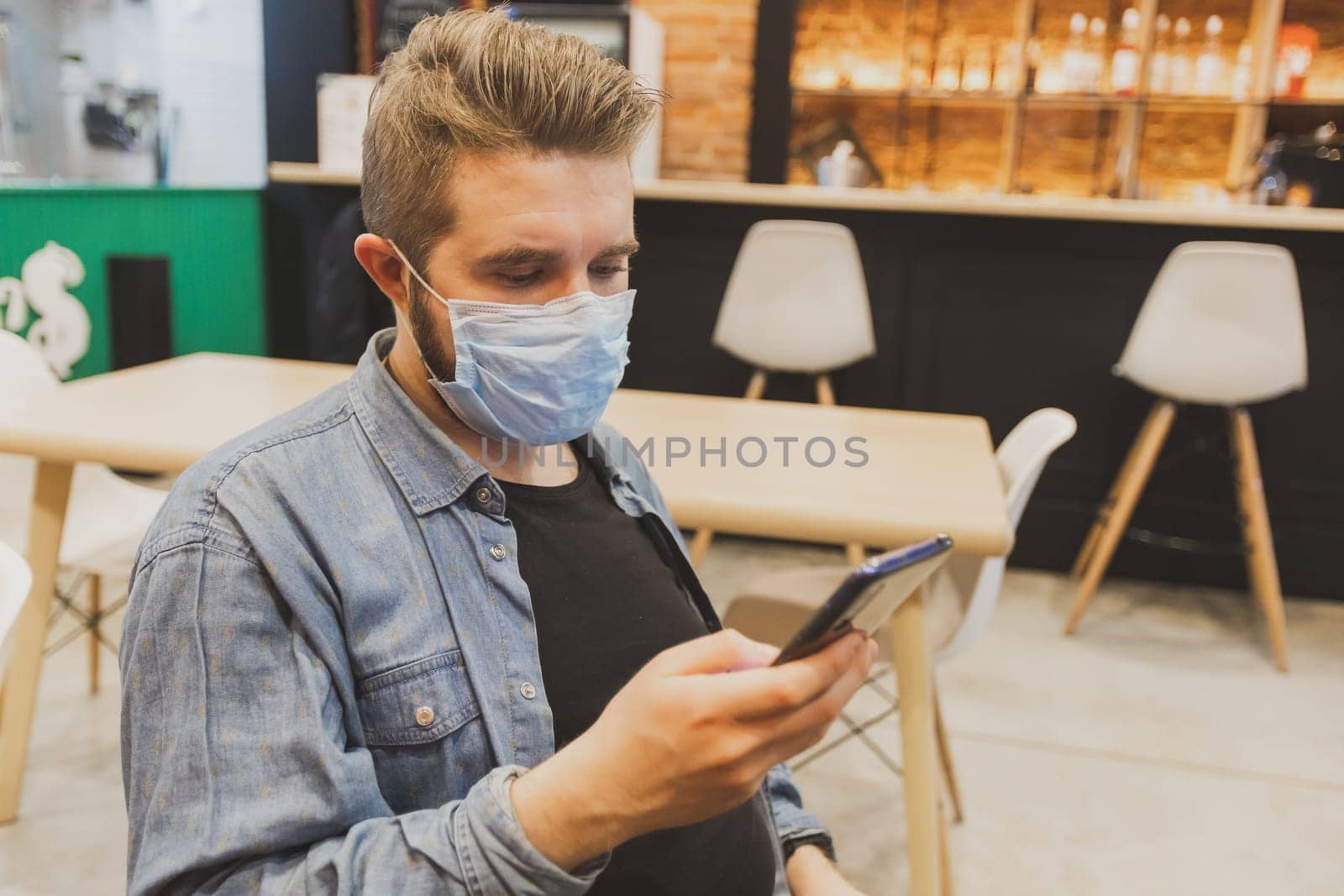 Man wears medical face mask in public area and using smartphone to do work business and social network communication in public cafe work space area