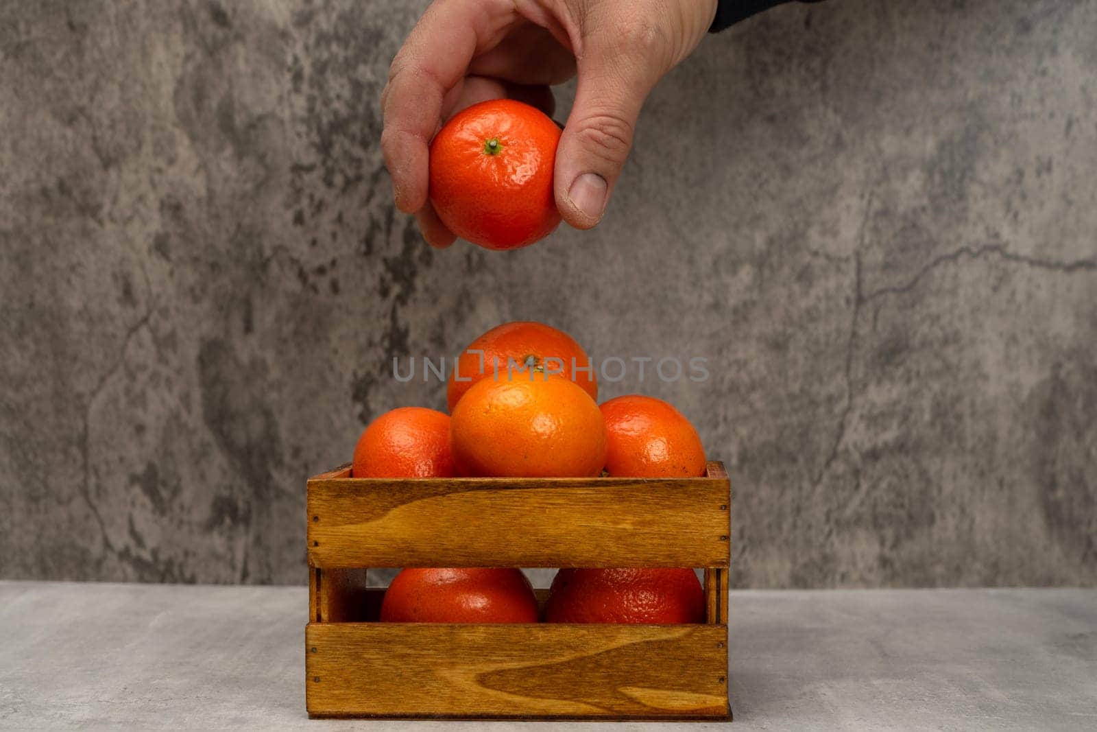 Man's hand picking an orange from a beautiful wooden basket with some ripe oranges in a still life with gray background, healthy living concept. Superfood rich in vitamin C.