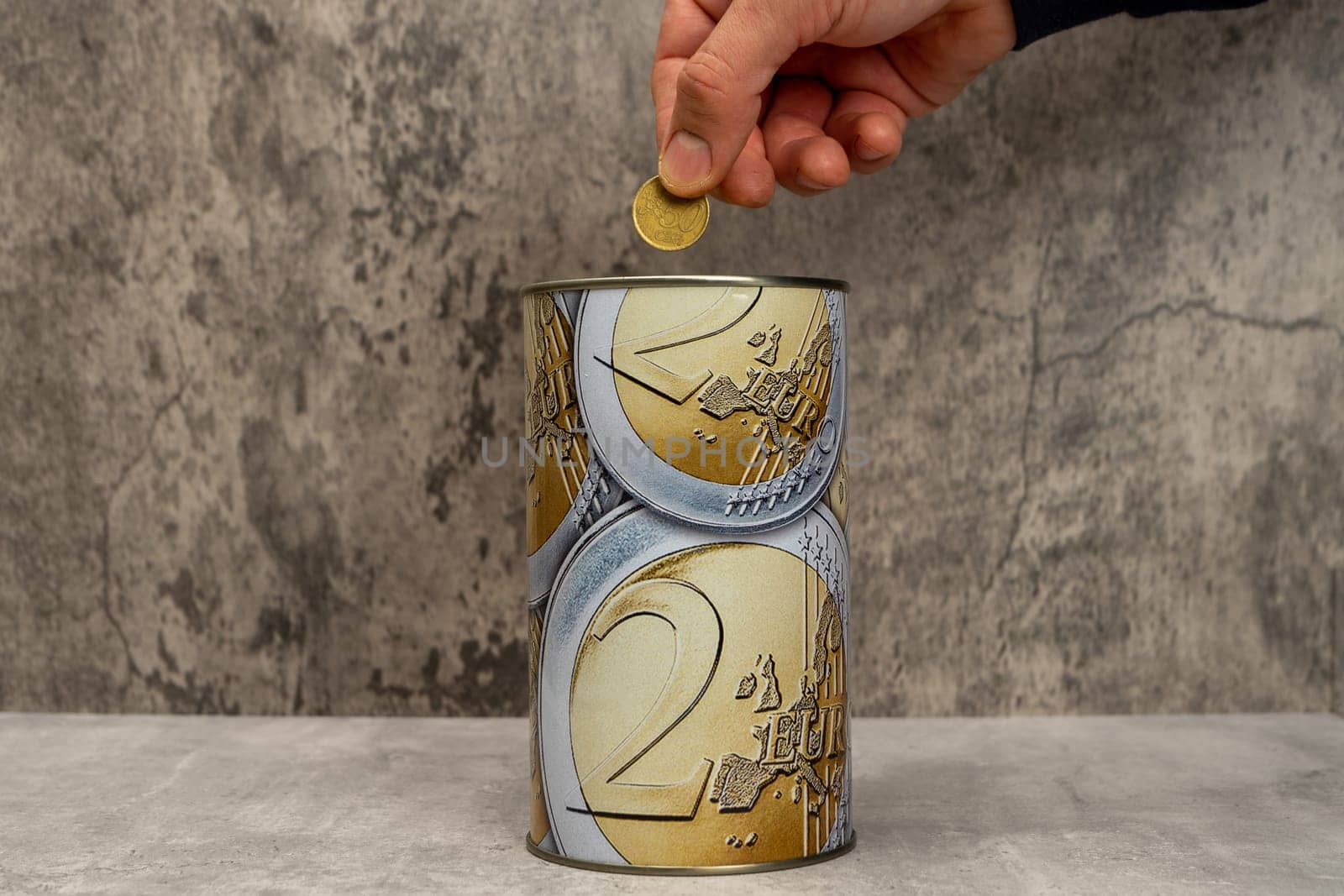 Man's hand putting a 50 cent coin into a metal piggy bank with euro symbols to save money. On a gray background. Keep bills in a makeshift savings account