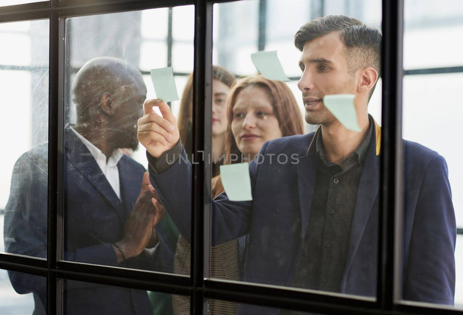 Creative business team looking at sticky notes on glass window