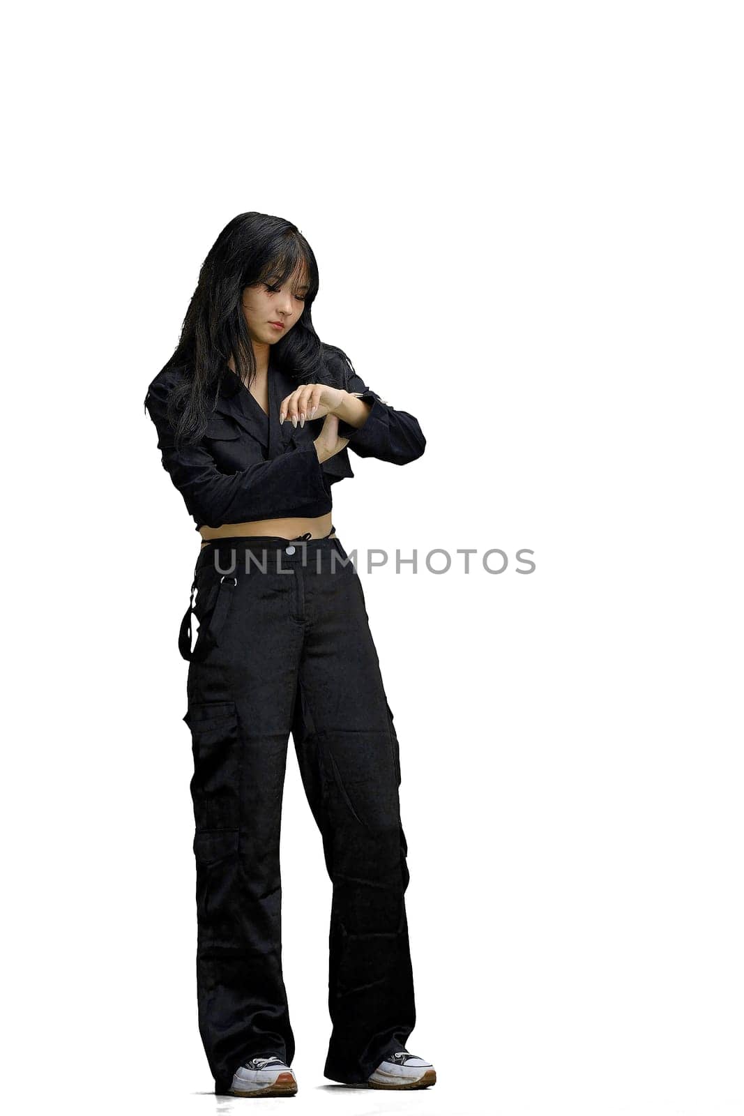 A woman in black clothes, on a white background, in full height, looks at her watch.