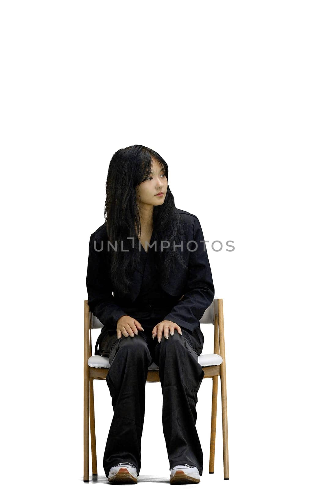 A woman in black clothes, on a white background, is sitting on a chair.