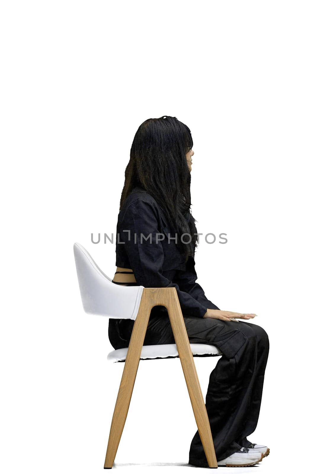 A woman in black clothes, on a white background, is sitting on a chair.