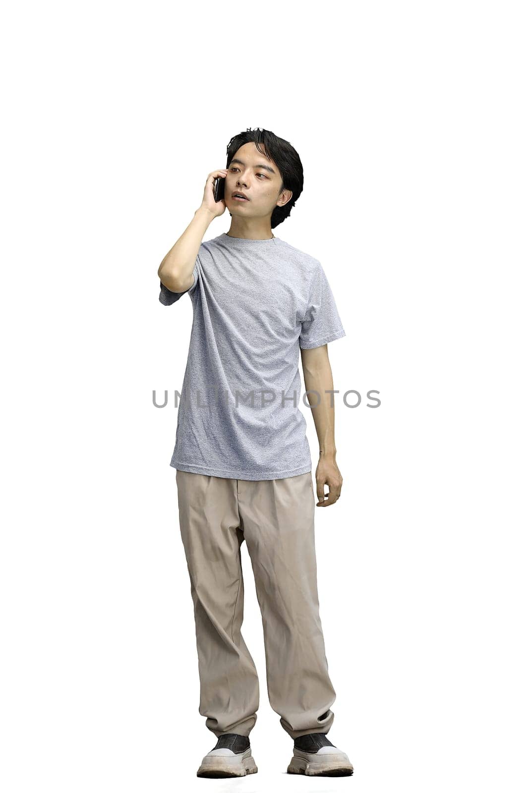 A guy in a gray T-shirt, on a white background, full-length, talking on the phone.