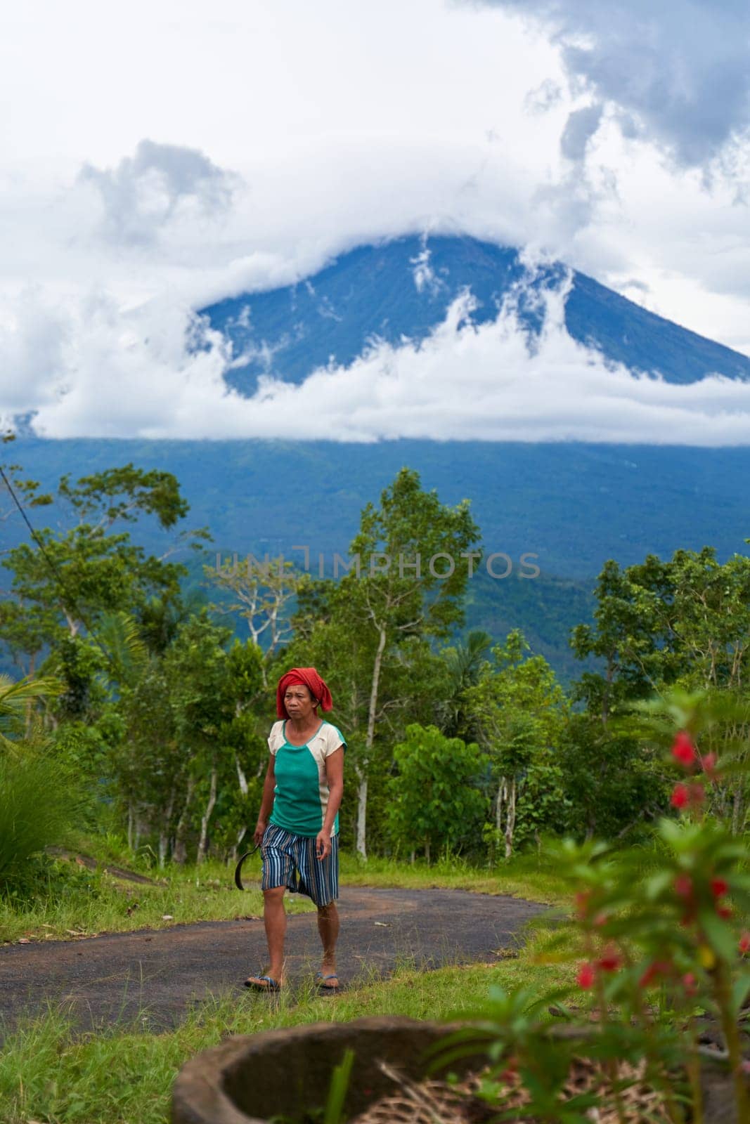 An old Asian woman drives on a road in the mountains with a view of the popular holy volcano Agung, shrouded in clouds on the island of Bali. by Try_my_best