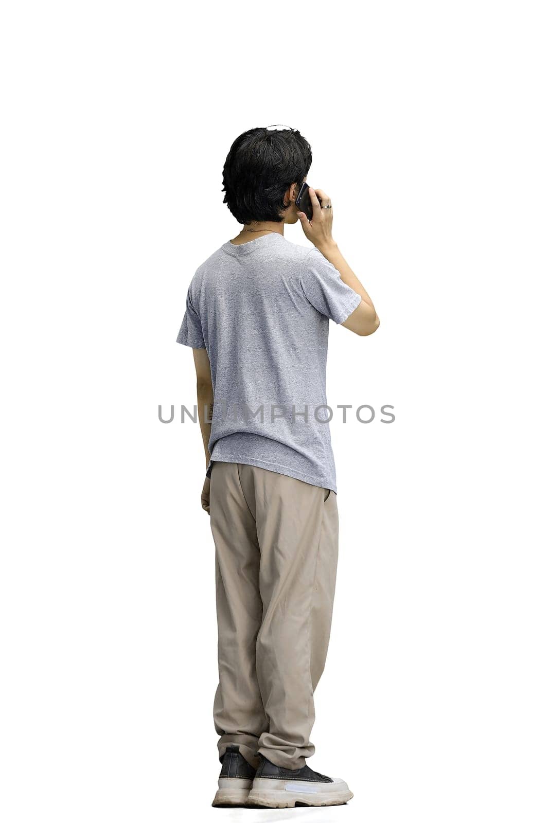 A guy in a gray T-shirt, on a white background, full-length, talking on the phone.