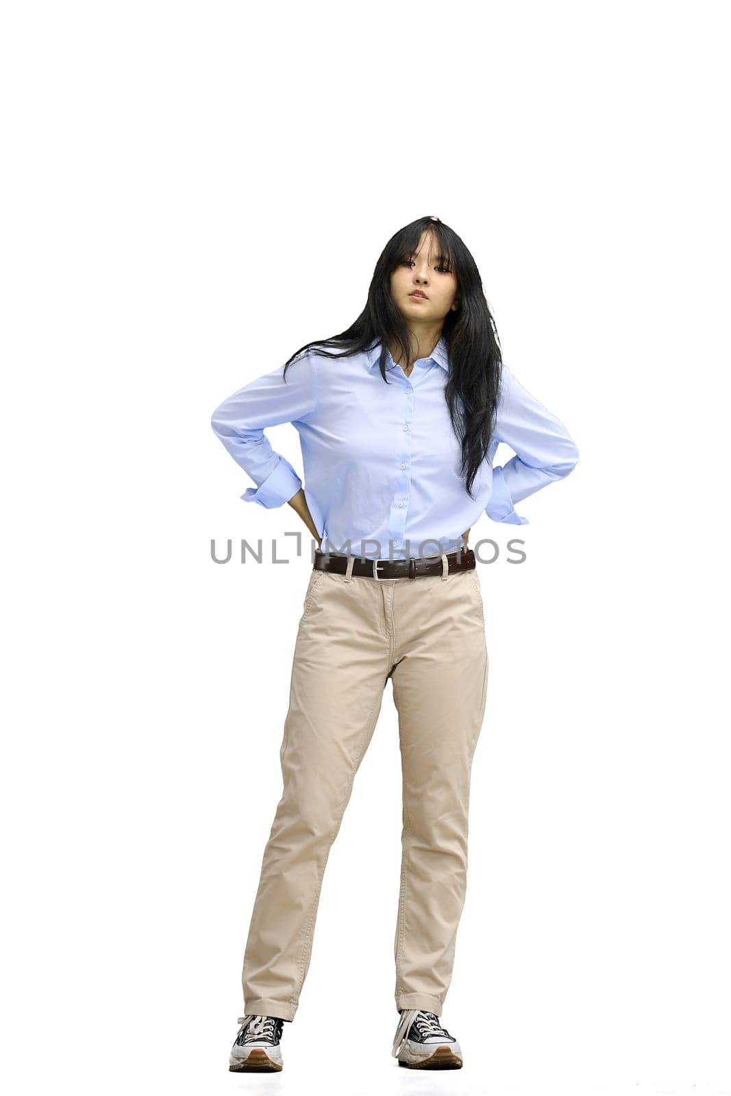 A girl in a blue shirt, on a white background, full-length, hands on her belt.