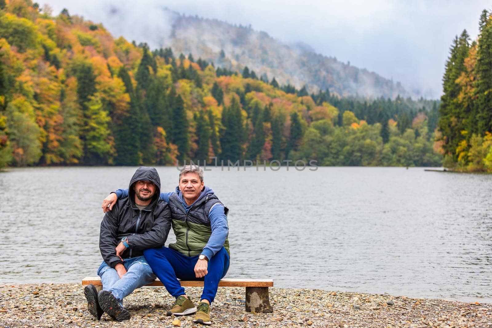 Two friends enjoy the view of a mountain lake surrounded by brightly colored trees