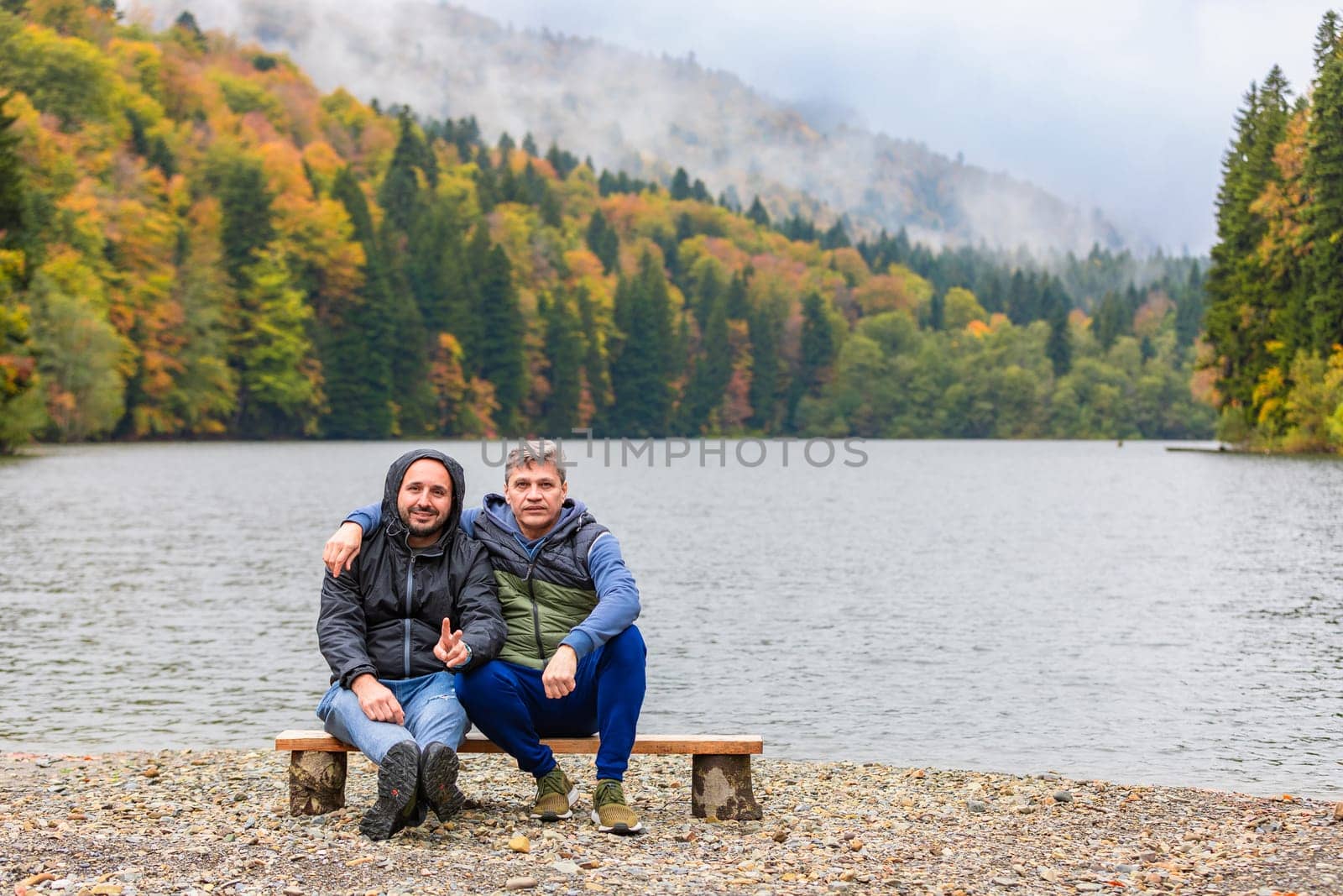 The autumn landscape of a lake in the mountains becomes a place of retreat for two men enjoying the beautiful view and tranquility of nature.